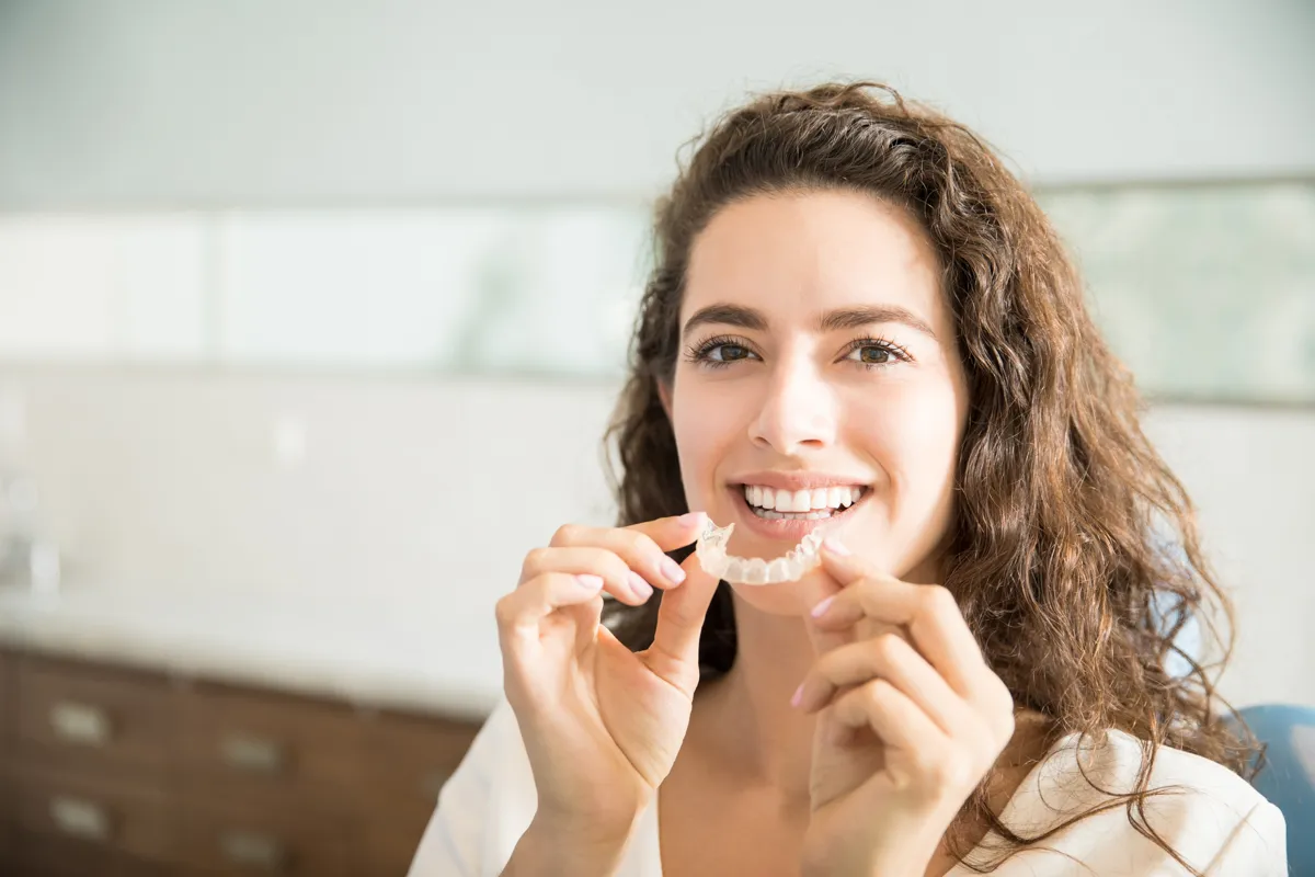 Smiling patient holding a clear aligner in the clinic